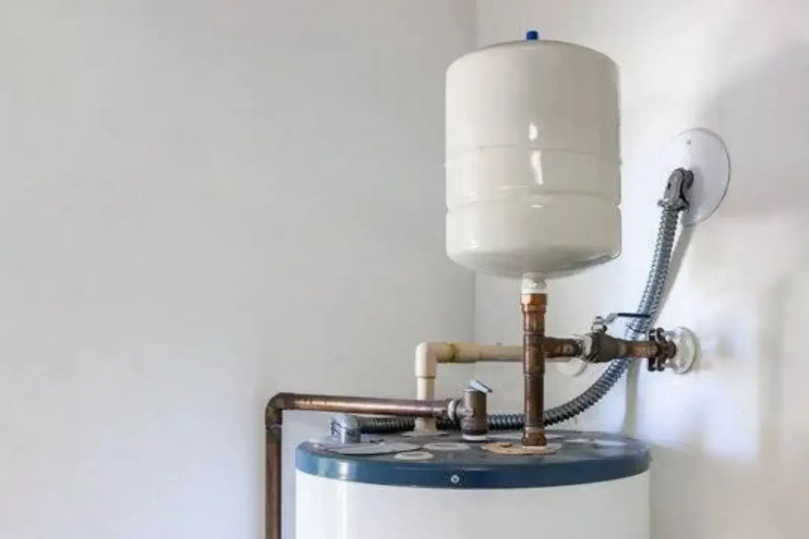 White expansion tank mounted on copper piping above a water heater