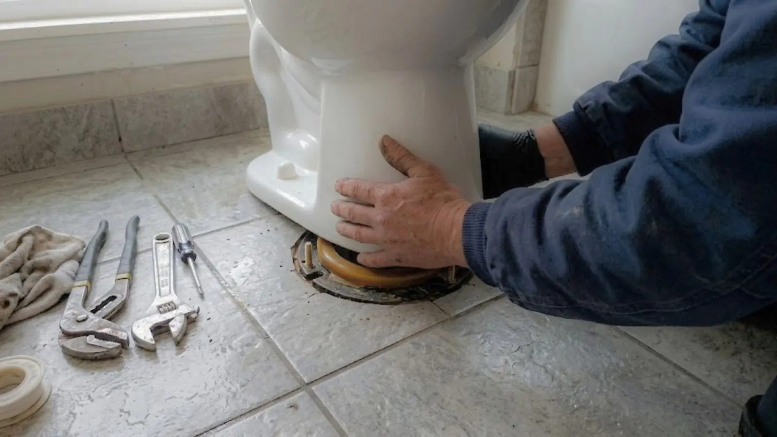 Hands setting a toilet onto the wax ring and flange on a tile floor