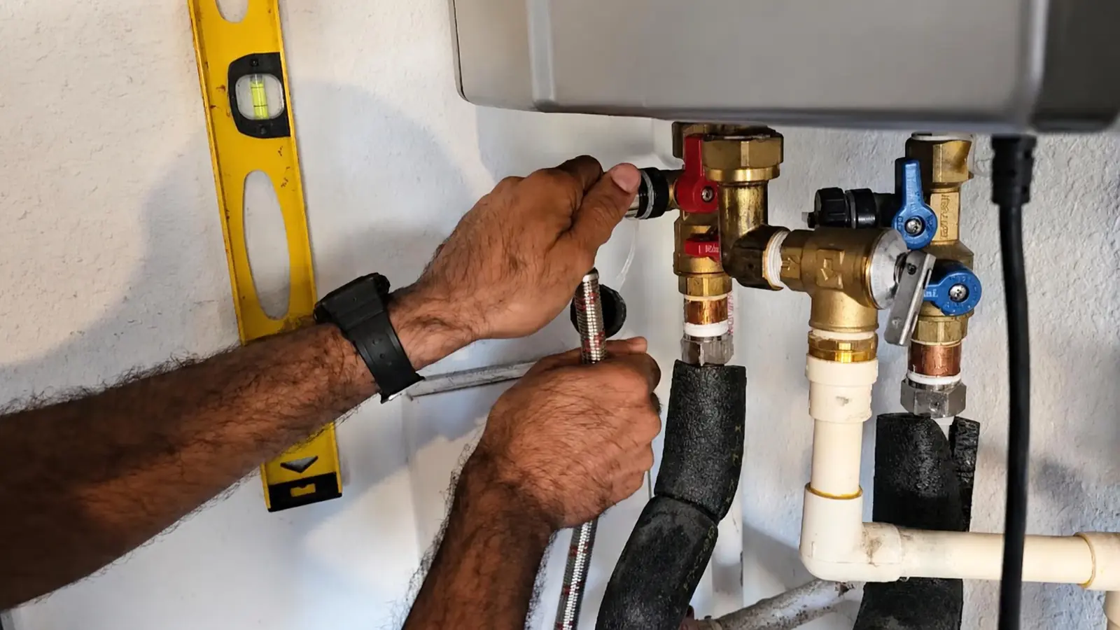 Hands connecting valves and flexible lines under a wall mounted tankless water heater