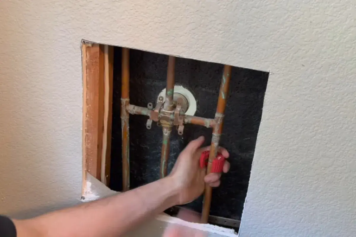 Hand reaching into an open wall to work on a copper shower valve
