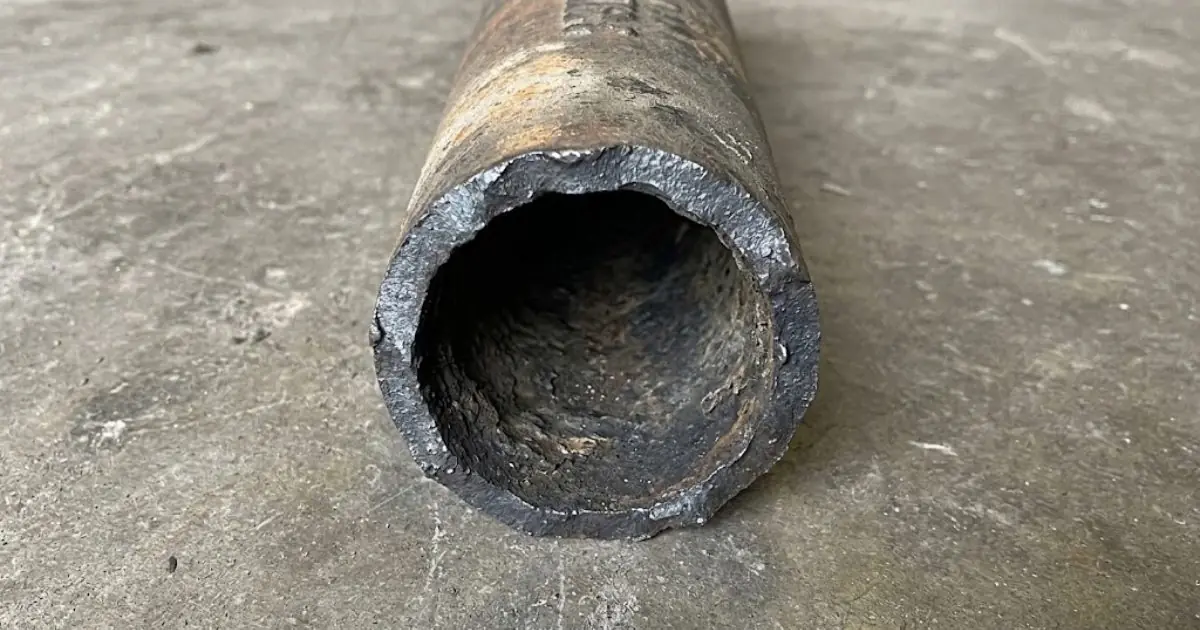 Cut section of old cast iron pipe showing a rough corroded interior on concrete