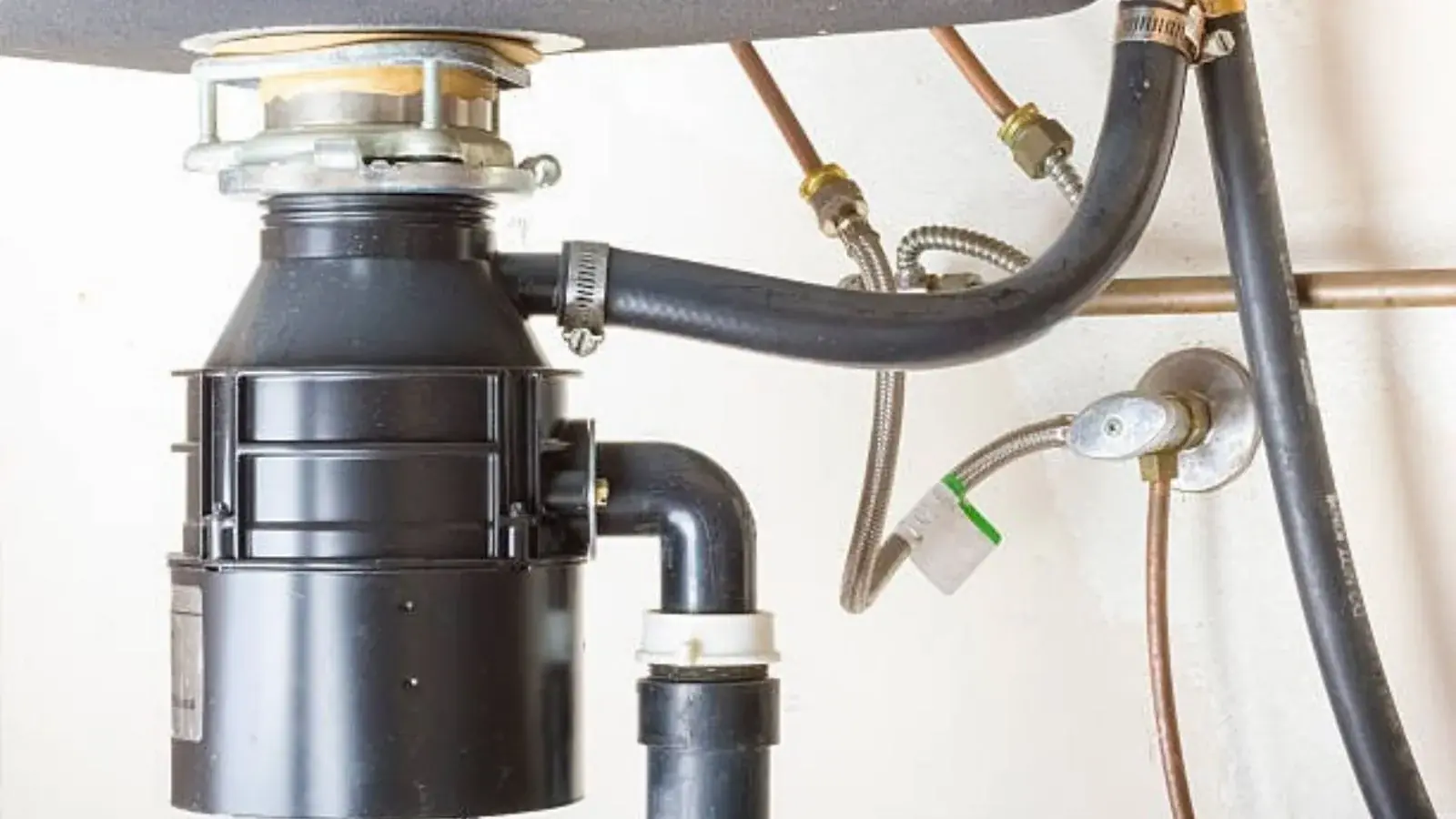 Garbage disposal mounted under a kitchen sink with hoses and drain pipe connected